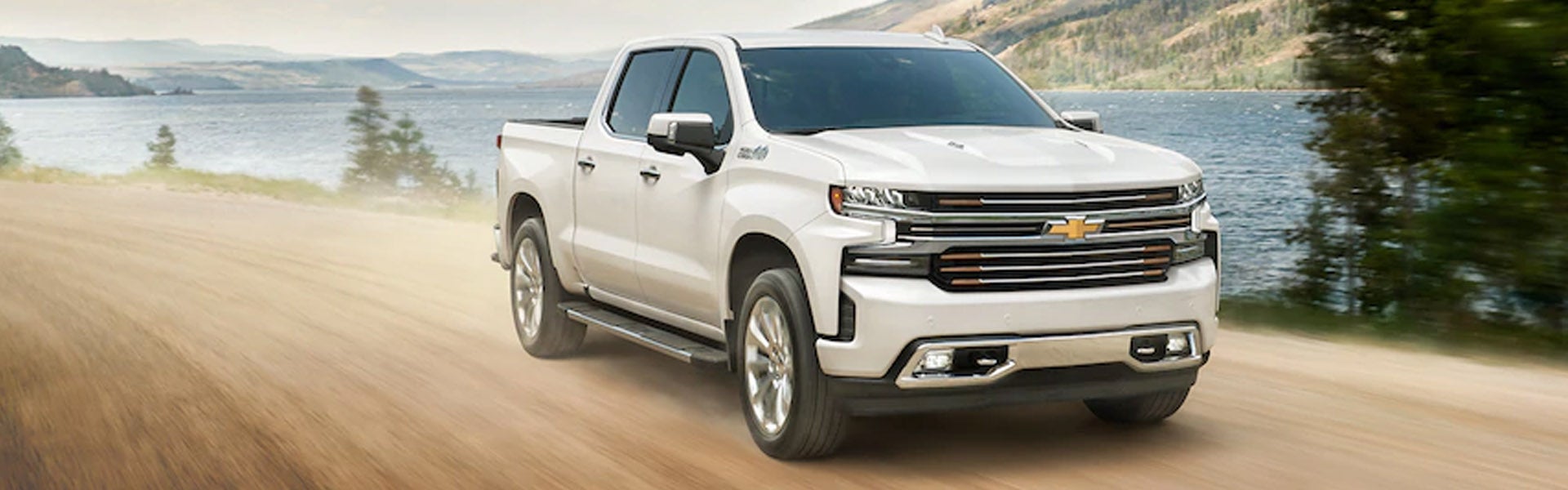 White 2020 Chevrolet Silverado 1500 driving on a dirt road by a lake