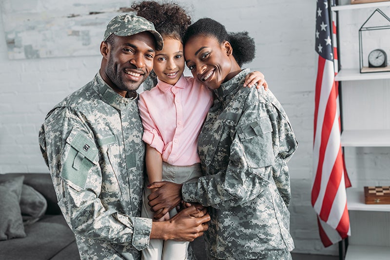 Military Couple Holding Their Daughter In Hands Stood In Front Of A Wall